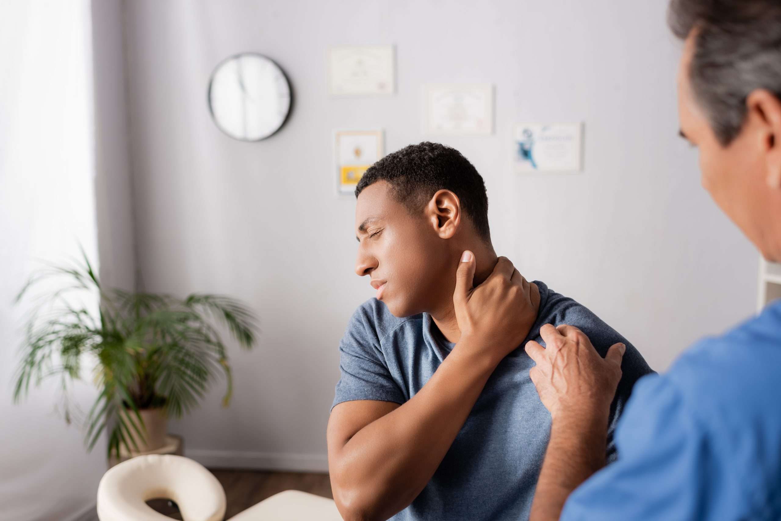 injured african american man touching neck near doctor on blurre