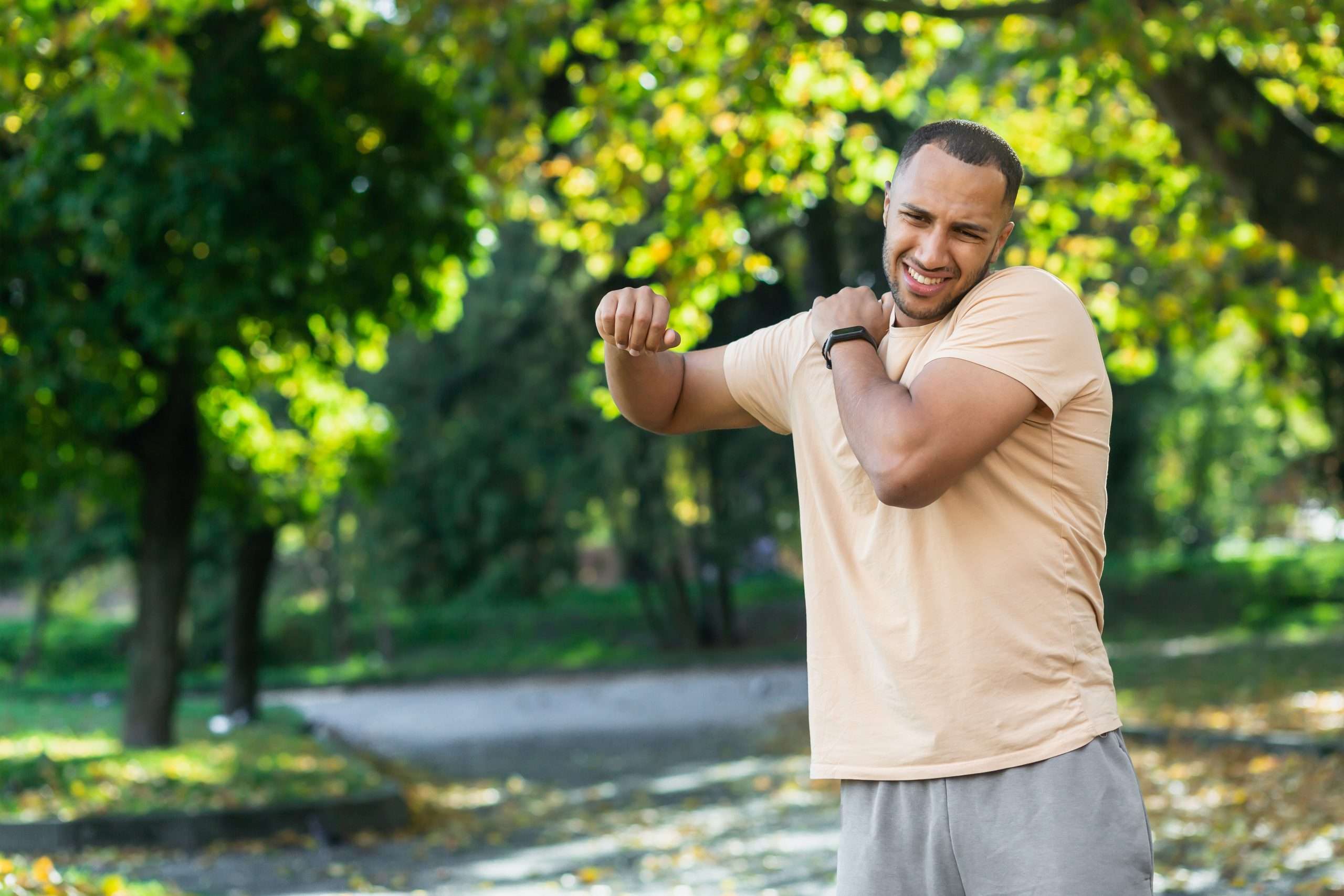 a man injured his shoulder during a fitness class, an african american man injured himself while jogging in the park, stretches his arm and massages his sore muscles