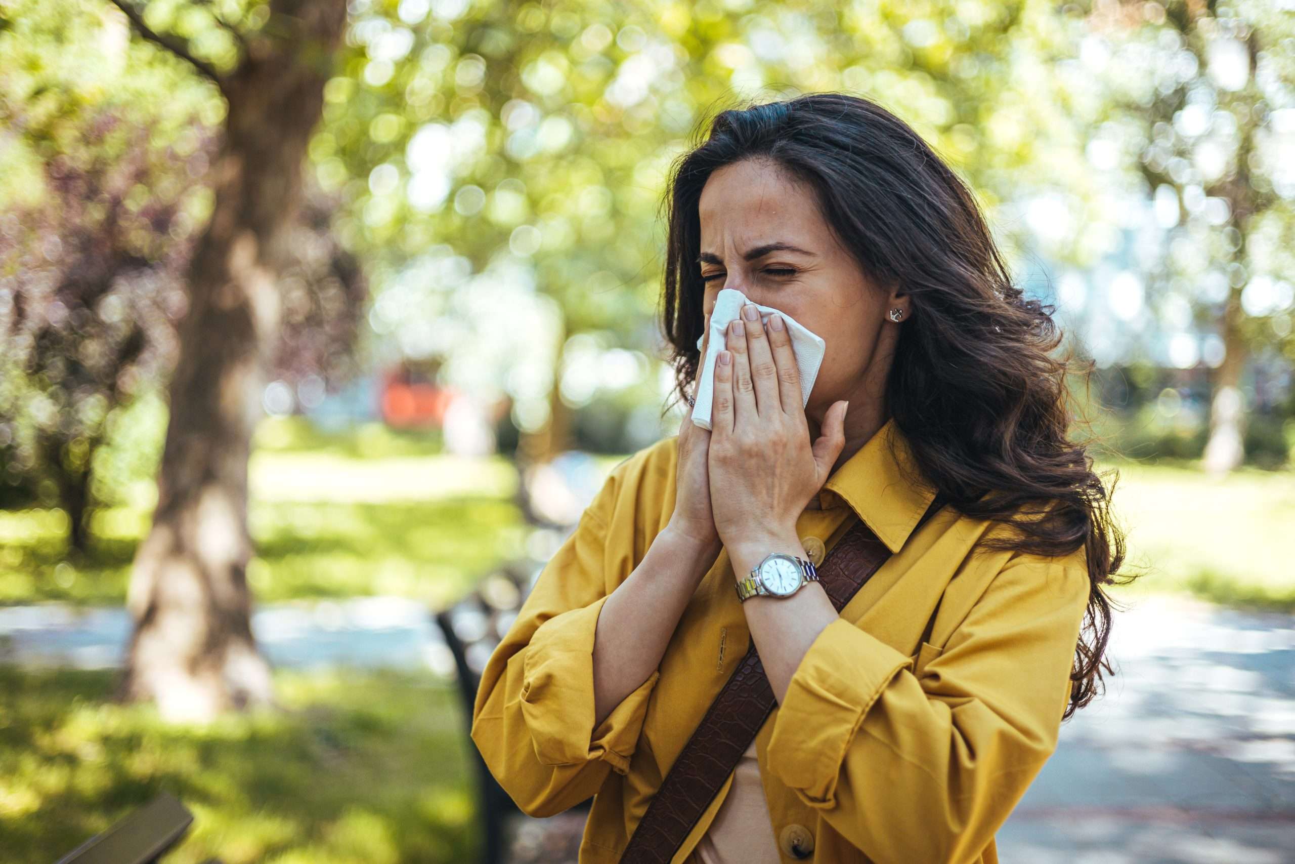 portrait of unhealthy cute female in yellow top with napkin blowing nose, looks to the source of the allergy, place for advertising. rhinitis, cold, allergy concept. pollen allergy symptoms